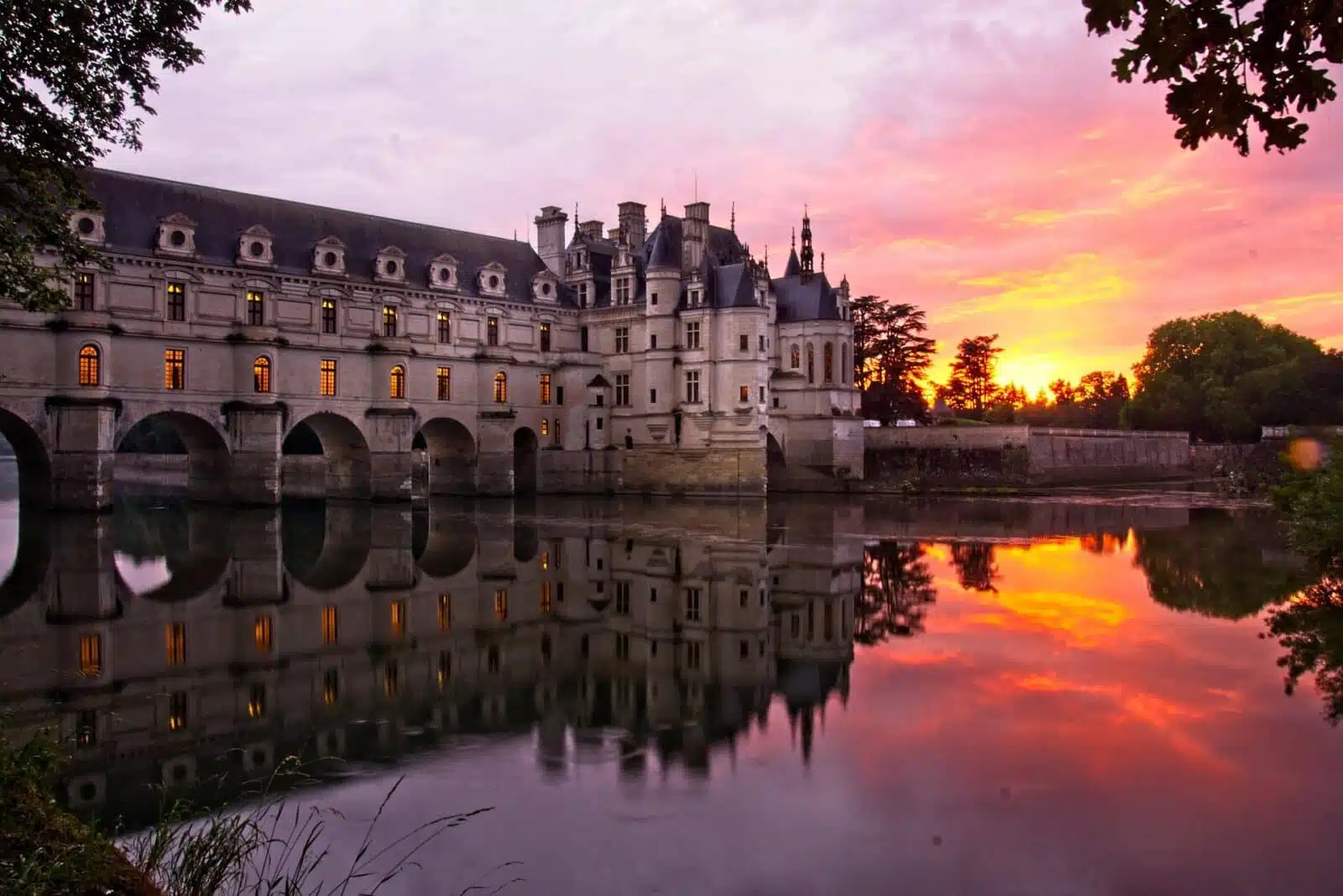 Vue du château de Chenonceau se reflétant dans le Cher au coucher du soleil